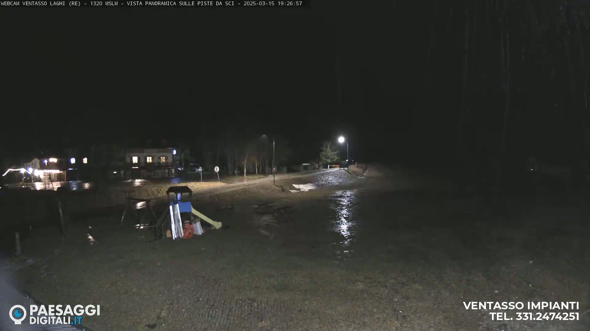 At night, under dark skies, a flooded area near a building and playground is illuminated by a streetlight.