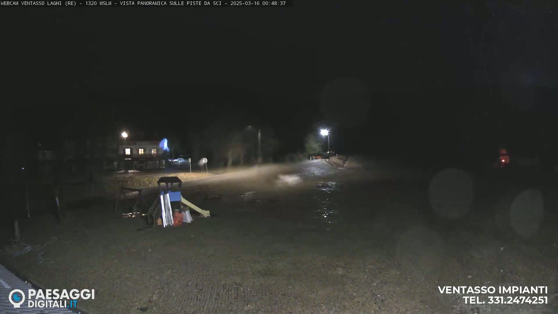 A nighttime scene shows a flooded road and playground equipment near a building under a dark sky.