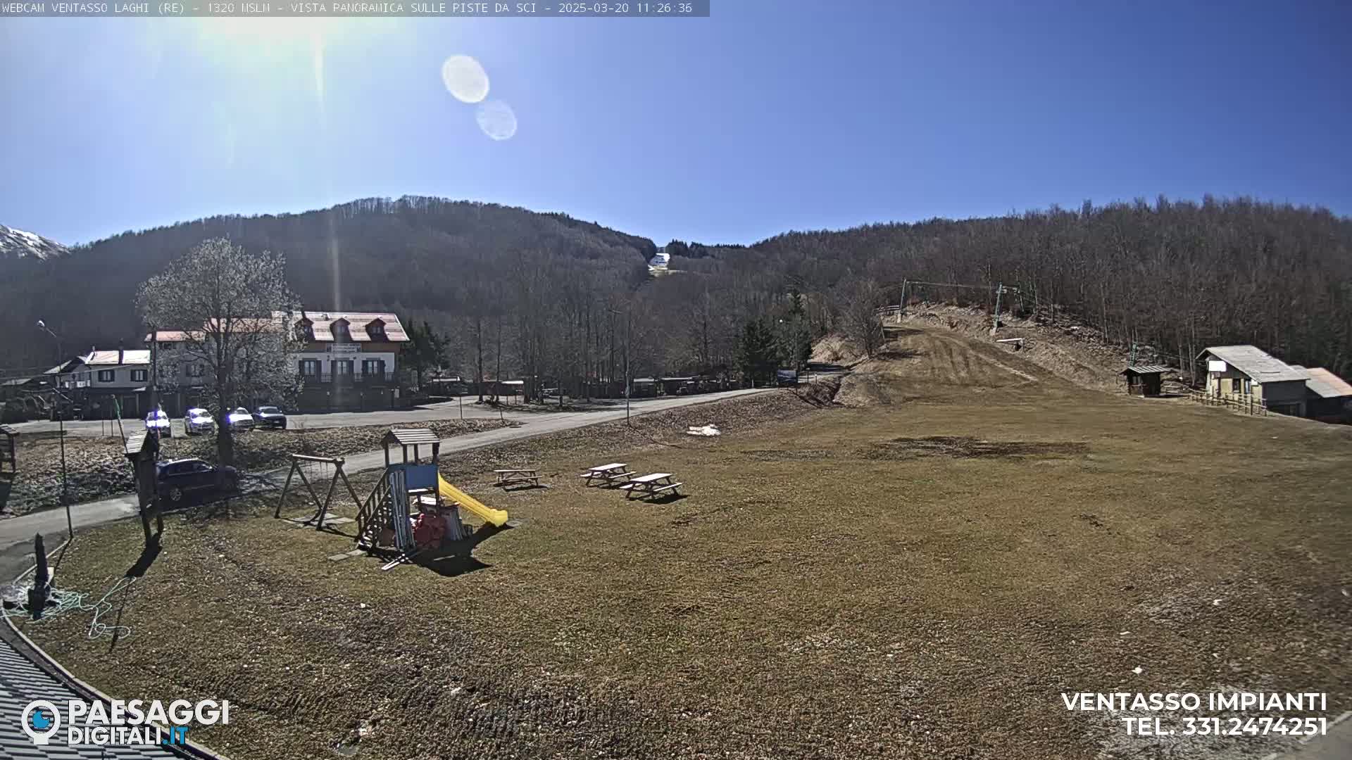 A sunny day reveals a playground, picnic tables, a building, and a ski slope in a mountainous area.