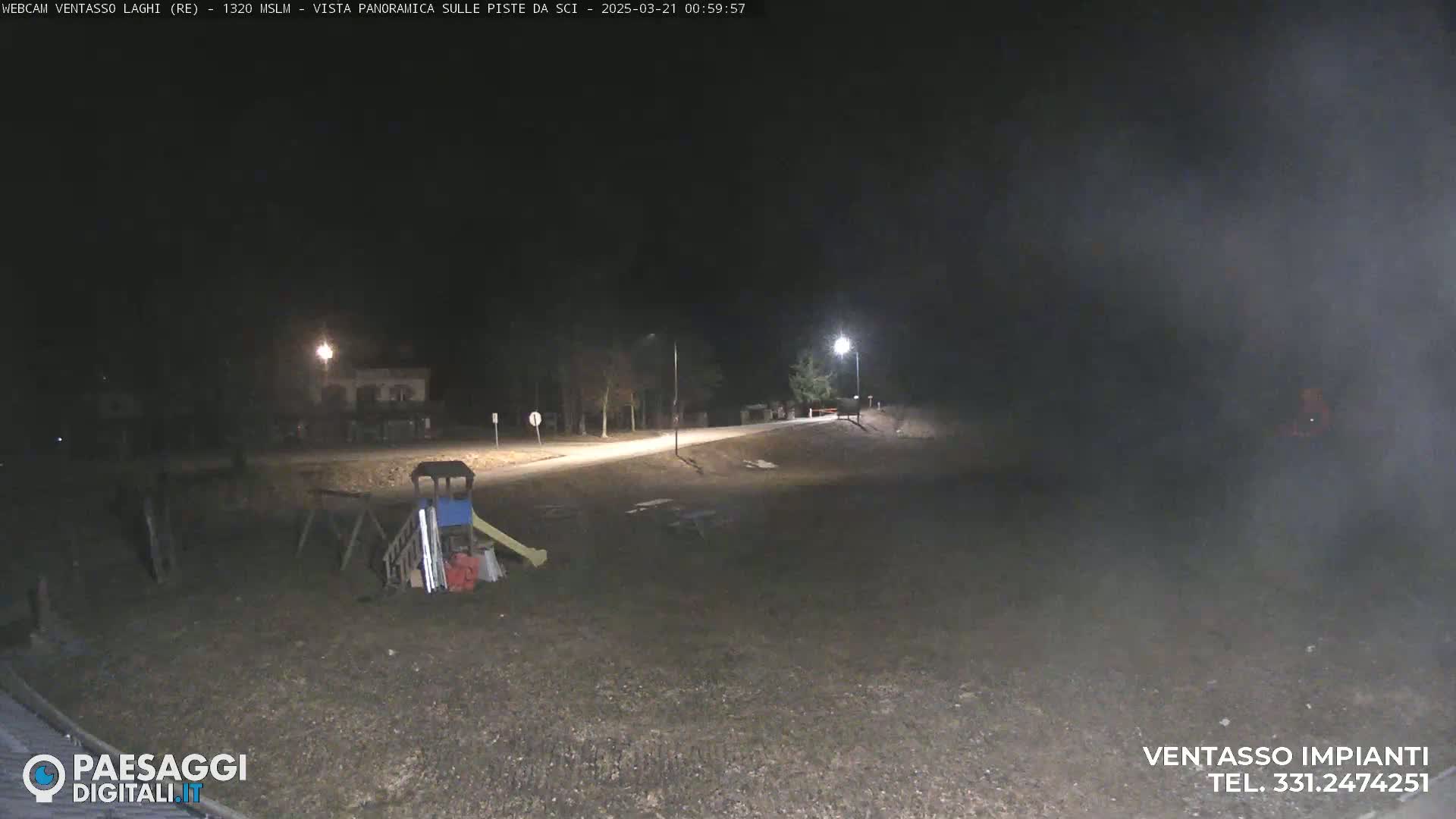 A nighttime, foggy view of an empty playground and a road with a few lights visible.