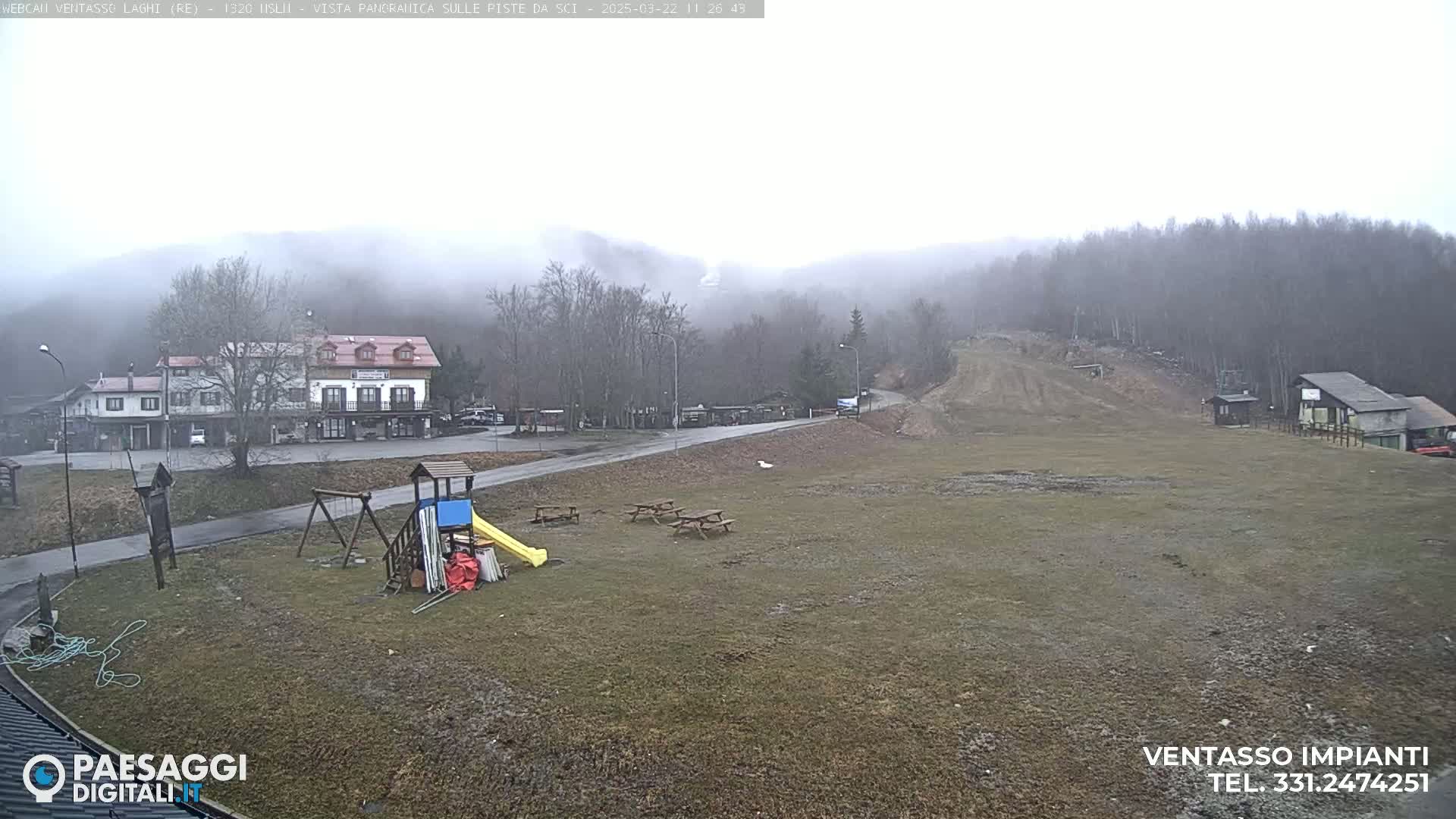 A foggy, overcast day reveals a playground, picnic tables, and buildings near a ski slope in a mountain valley.