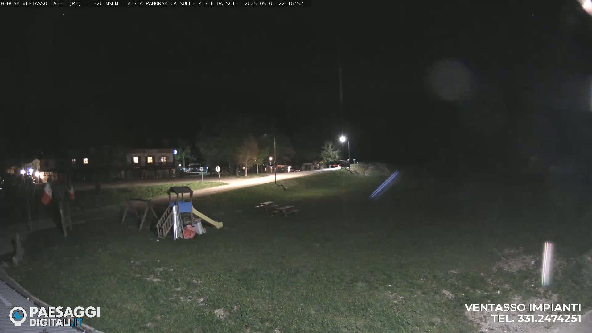 A nighttime view of an empty playground near a road and some buildings under a dark, clear sky.