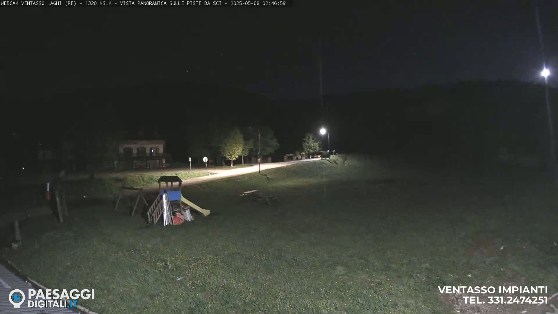 A nighttime view of a playground and picnic table near a road, illuminated by streetlights under a dark, clear sky.
