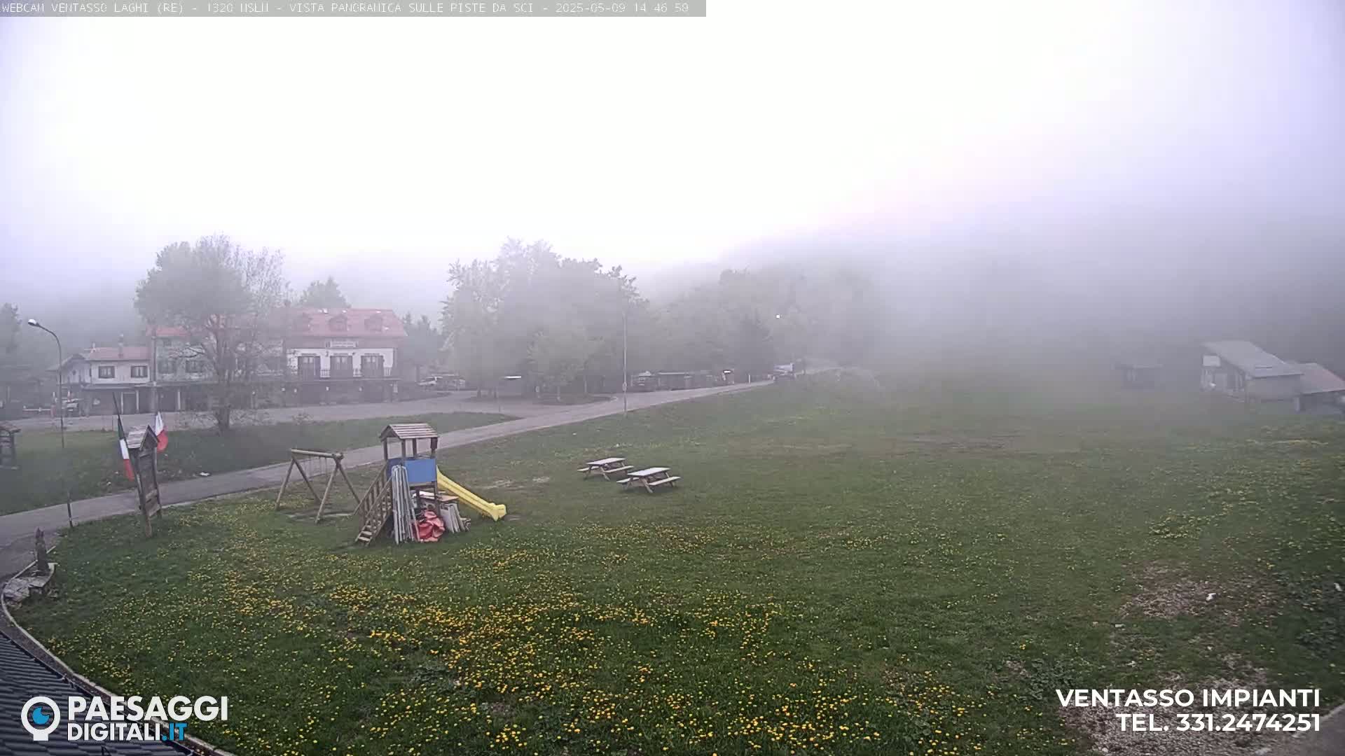 A foggy, grassy field with a playground, picnic tables, and buildings in the background.