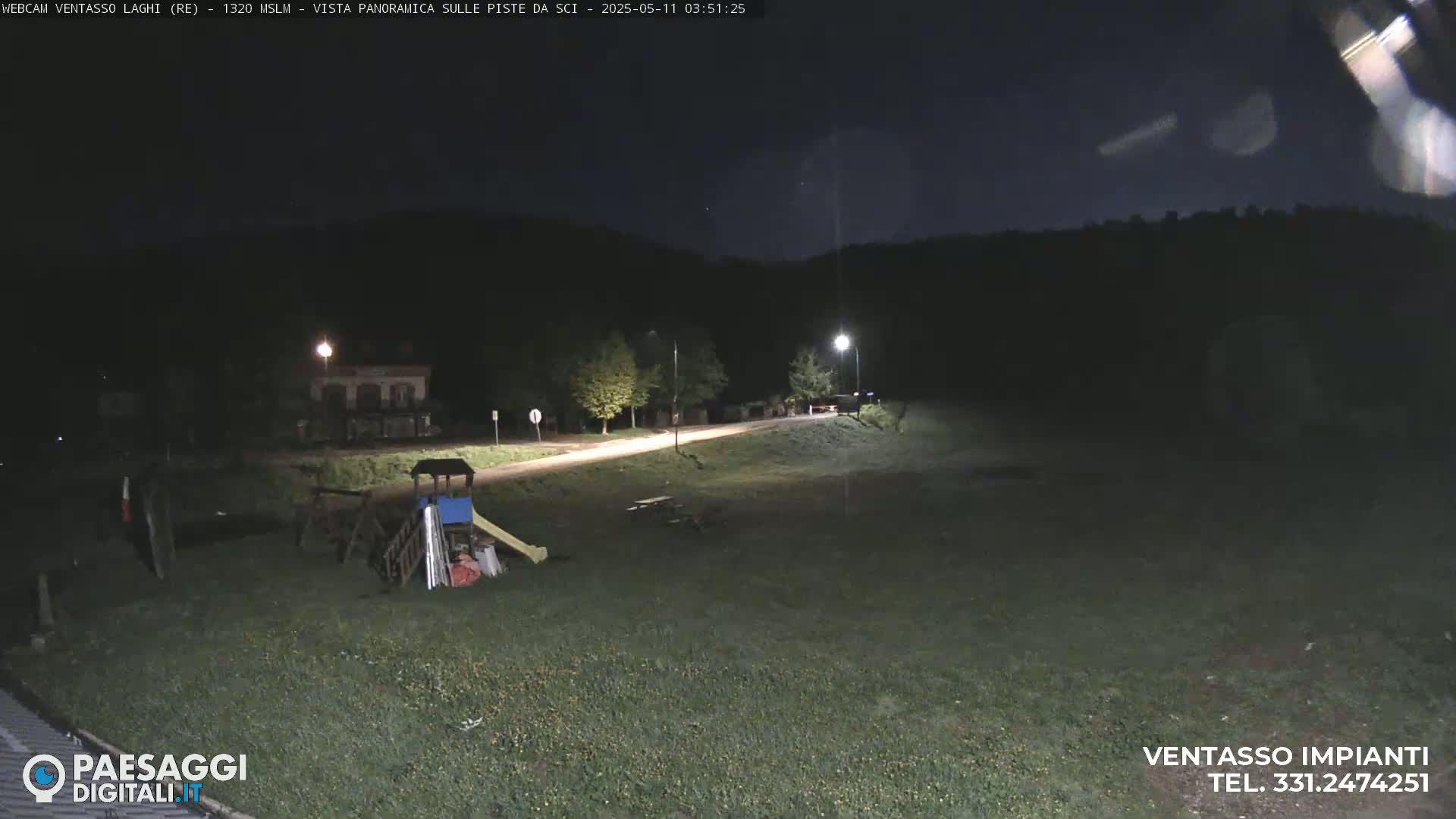 A nighttime view of a playground near a road, with a few streetlights illuminating the area under a dark sky.