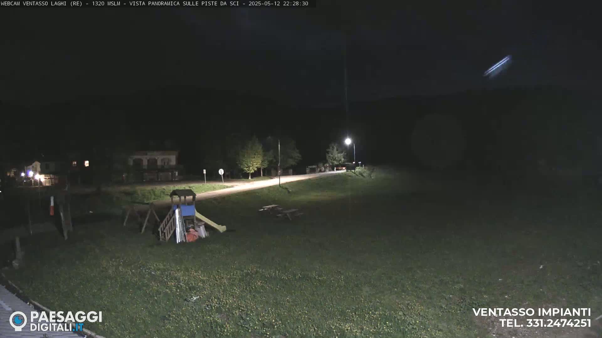 A nighttime view of a playground and picnic area near a road, under a clear, dark sky.