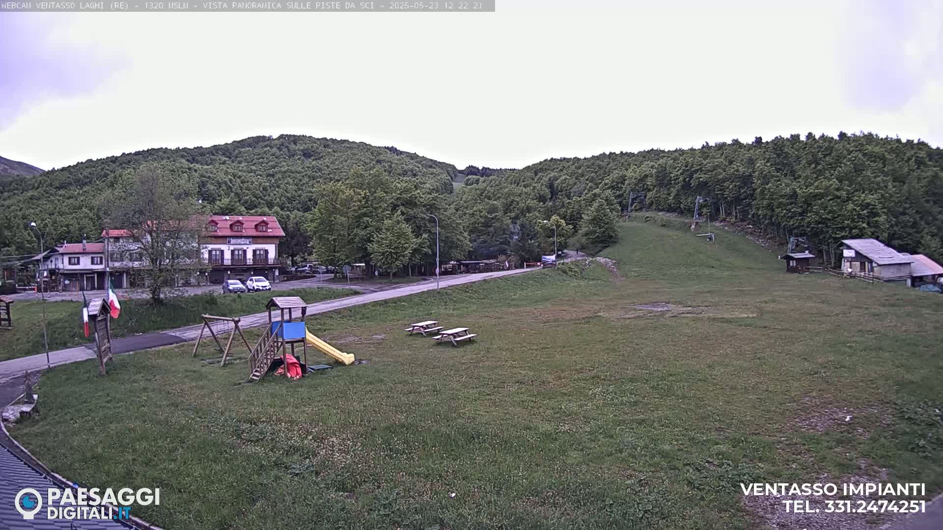 A playground and picnic tables sit in a grassy area near a building and a ski lift, all under an overcast sky.