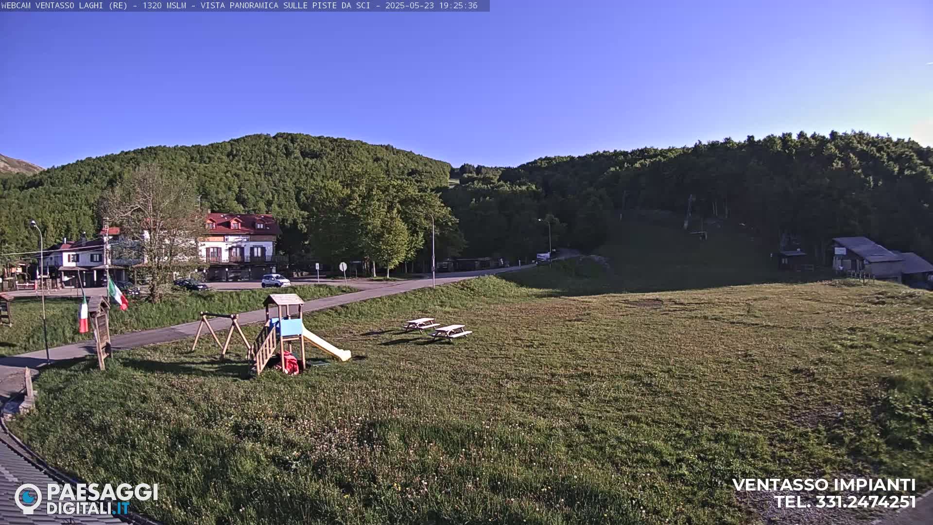 A grassy field with a playground, picnic tables, and a building in the background under a clear blue sky.