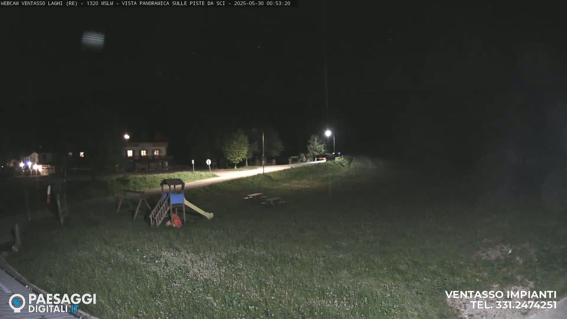 A nighttime, outdoor scene shows a playground, a road, and a building under a clear, dark sky.