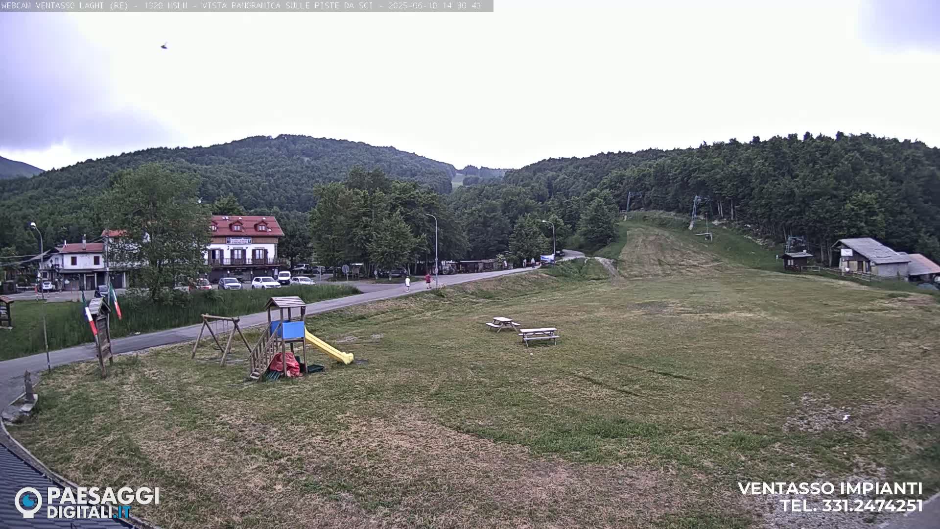 A mostly cloudy day overlooking a grassy area with a playground, buildings, and a ski slope in the background.