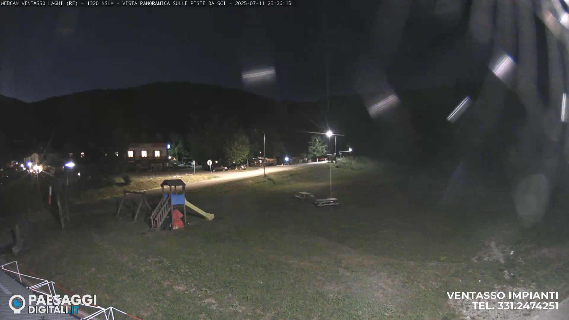 A nighttime view of a playground and a small road, with a building in the background under a clear, dark sky.