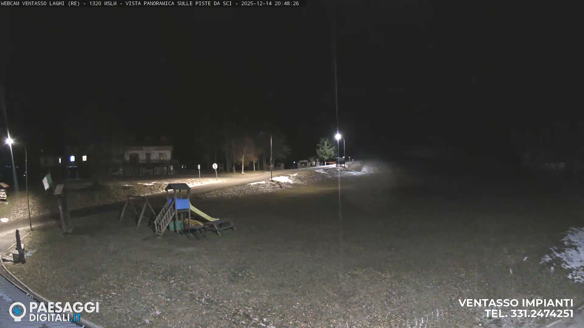 A foggy outdoor scene reveals a green field with patches of snow, a children's playground, and picnic tables in the foreground, leading to buildings and bare trees partially hidden by dense mist in the midground and background.