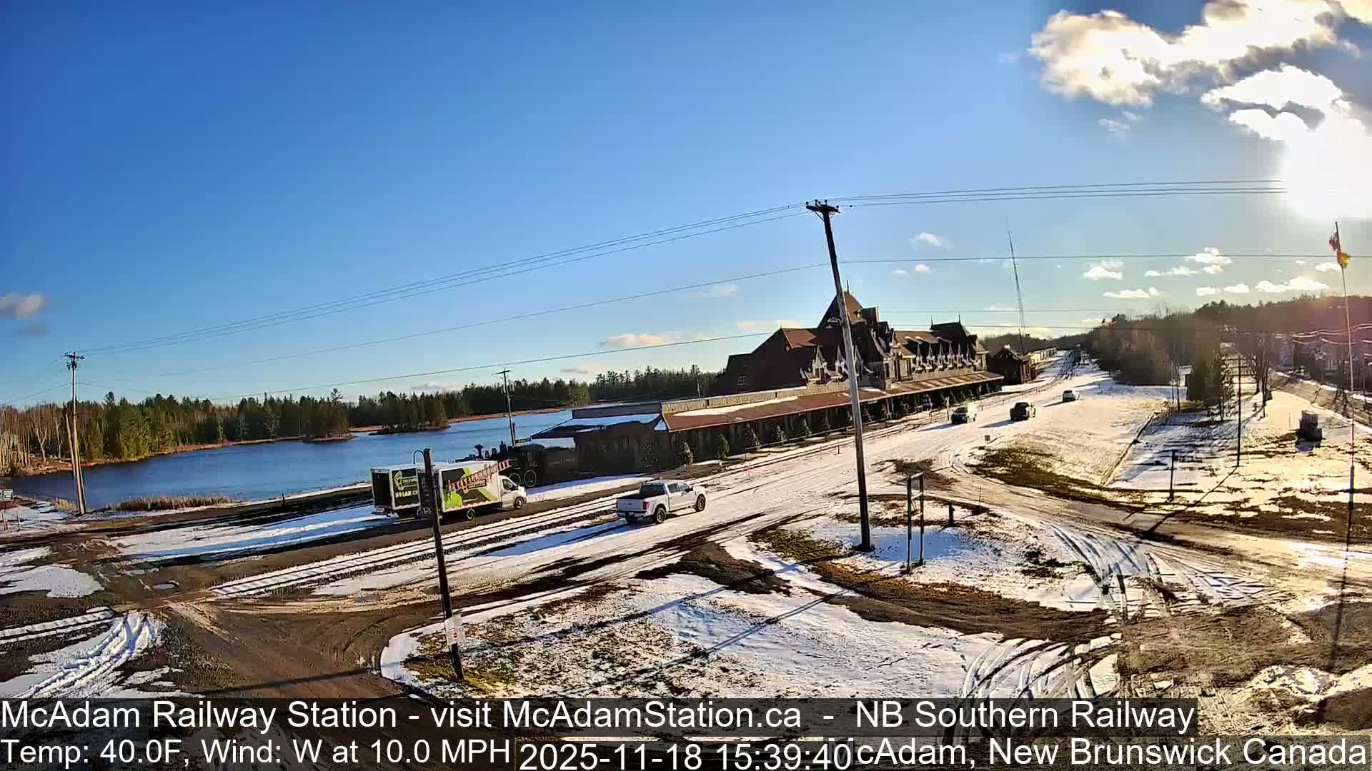 A brightly lit historic railway station, adorned with festive lights and featuring a parked locomotive on tracks, stands under a clear, cold night sky.