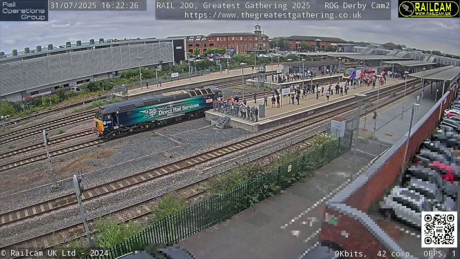 A train is arriving at a train station on an overcast day, with many people gathered to watch.