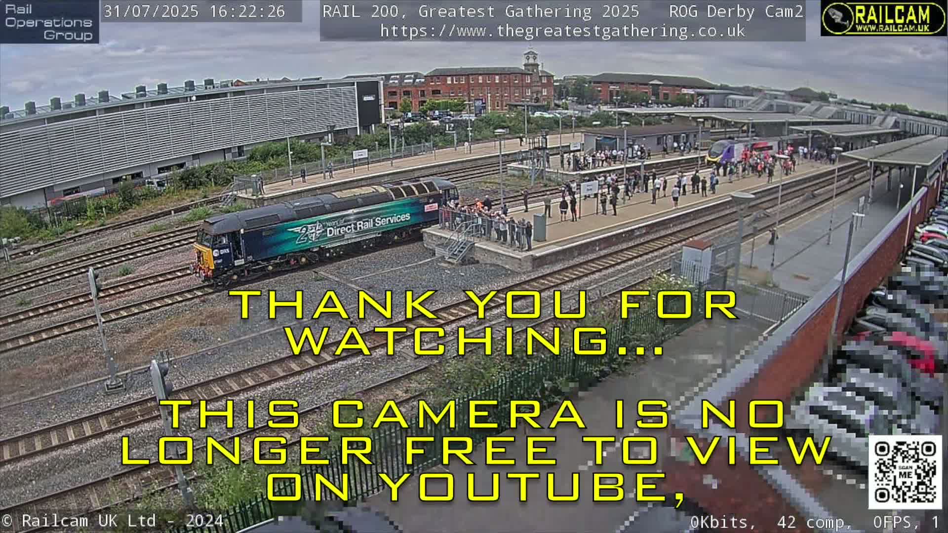 A train is arriving at a station platform where a crowd of people are gathered on a partly sunny day.