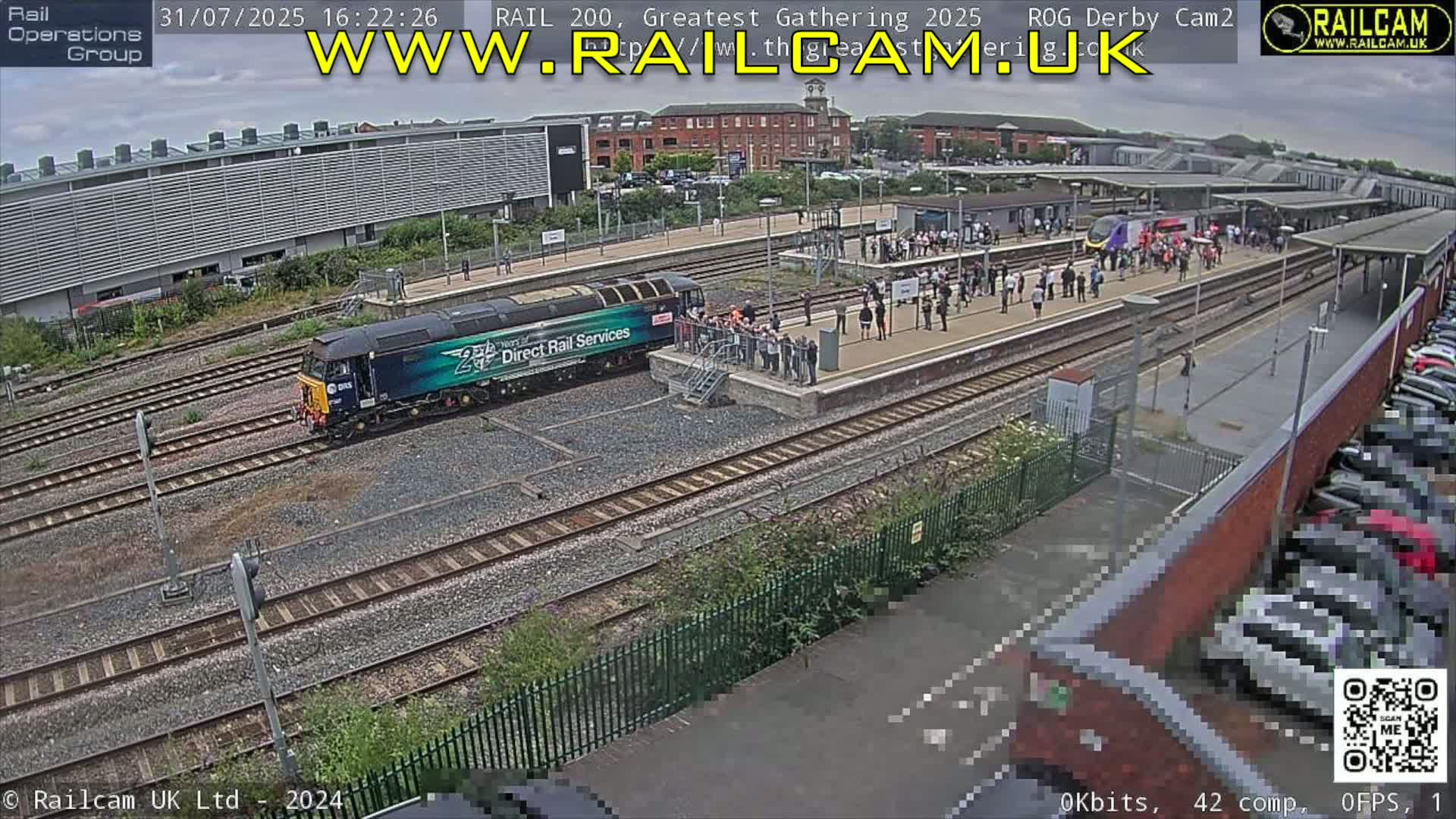 A train is at a station platform where many people are gathered on a partly cloudy day.