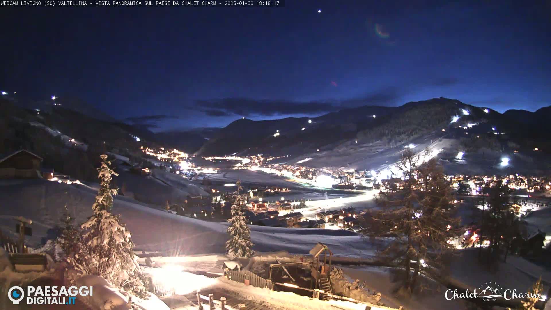 A snow-covered mountain village is illuminated at night under a dark blue, clear sky.