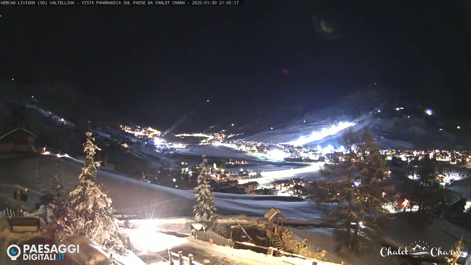 A snow-covered valley town is illuminated at night under a clear, dark sky.