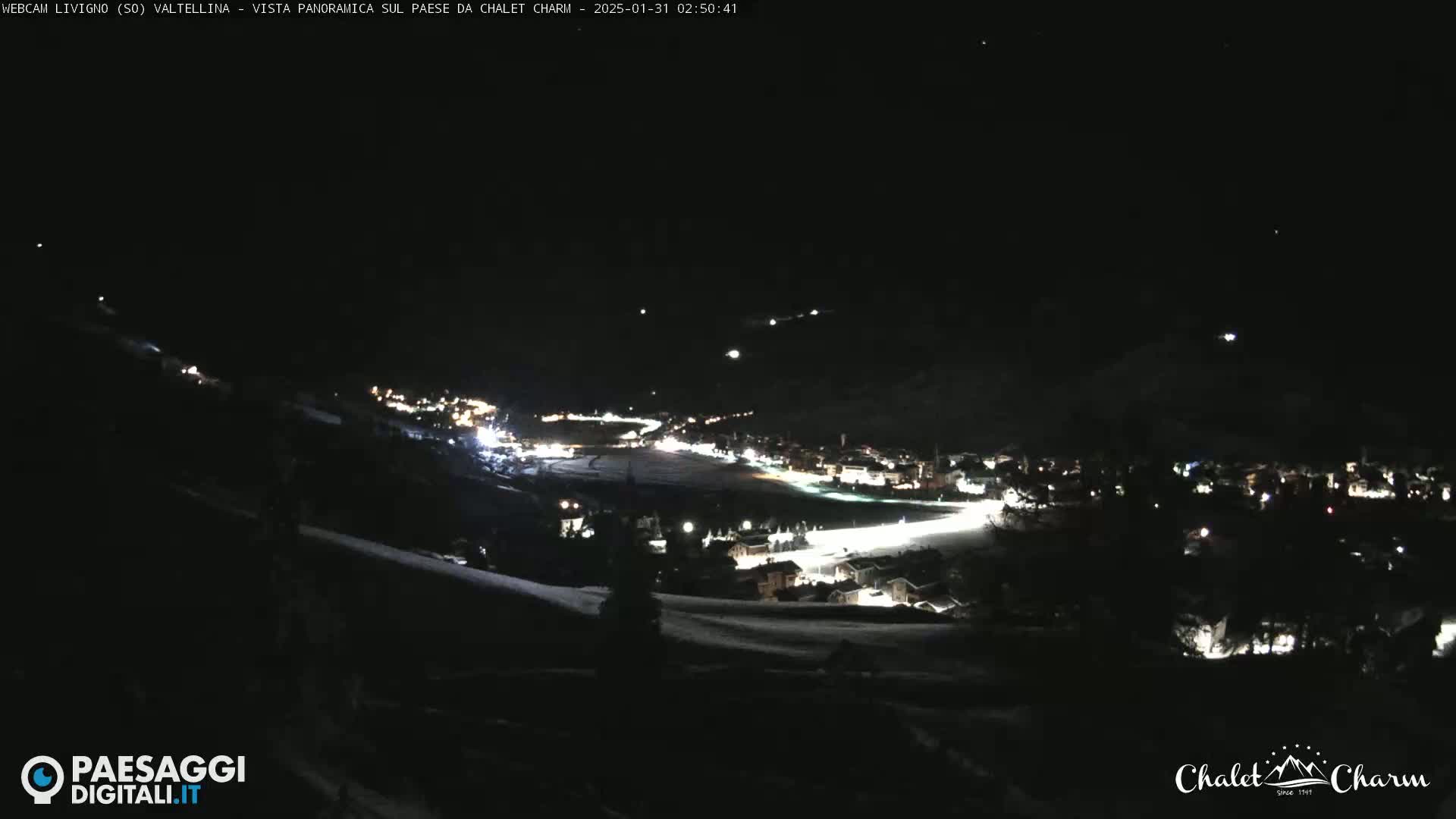 A nighttime, panoramic view of a snow-covered town with illuminated buildings under a clear, dark sky.