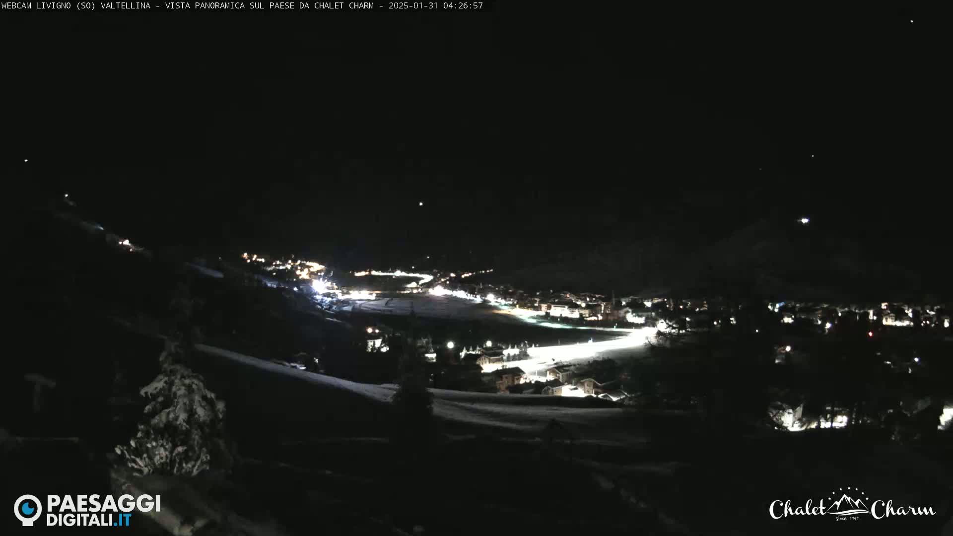 A nighttime panoramic view of a snow-covered town illuminated by lights, under a clear, dark sky.