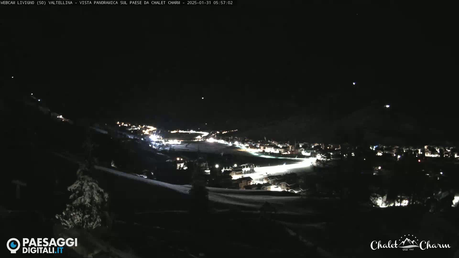A nighttime, panoramic view of a snow-covered town illuminated by lights, seen from a higher vantage point.
