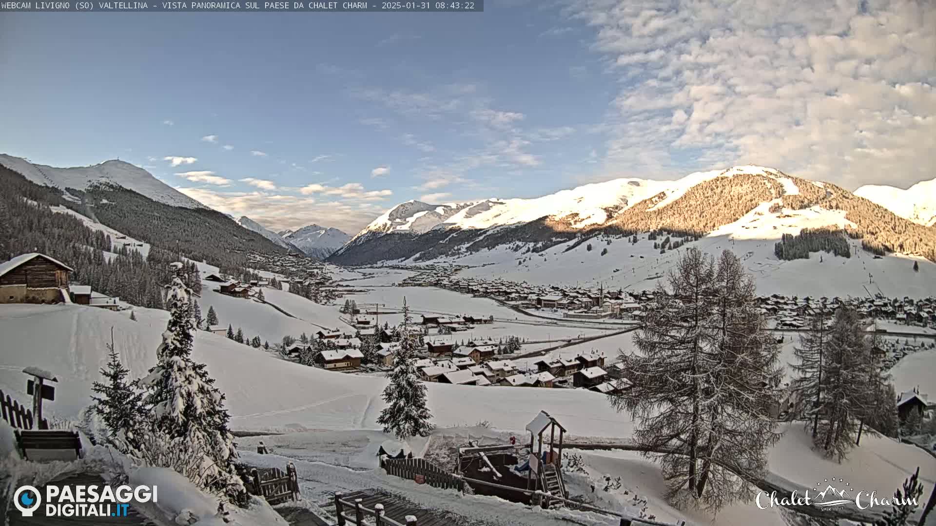 A snow-covered village nestled in a valley between snow-capped mountains under a mostly clear, bright sky.