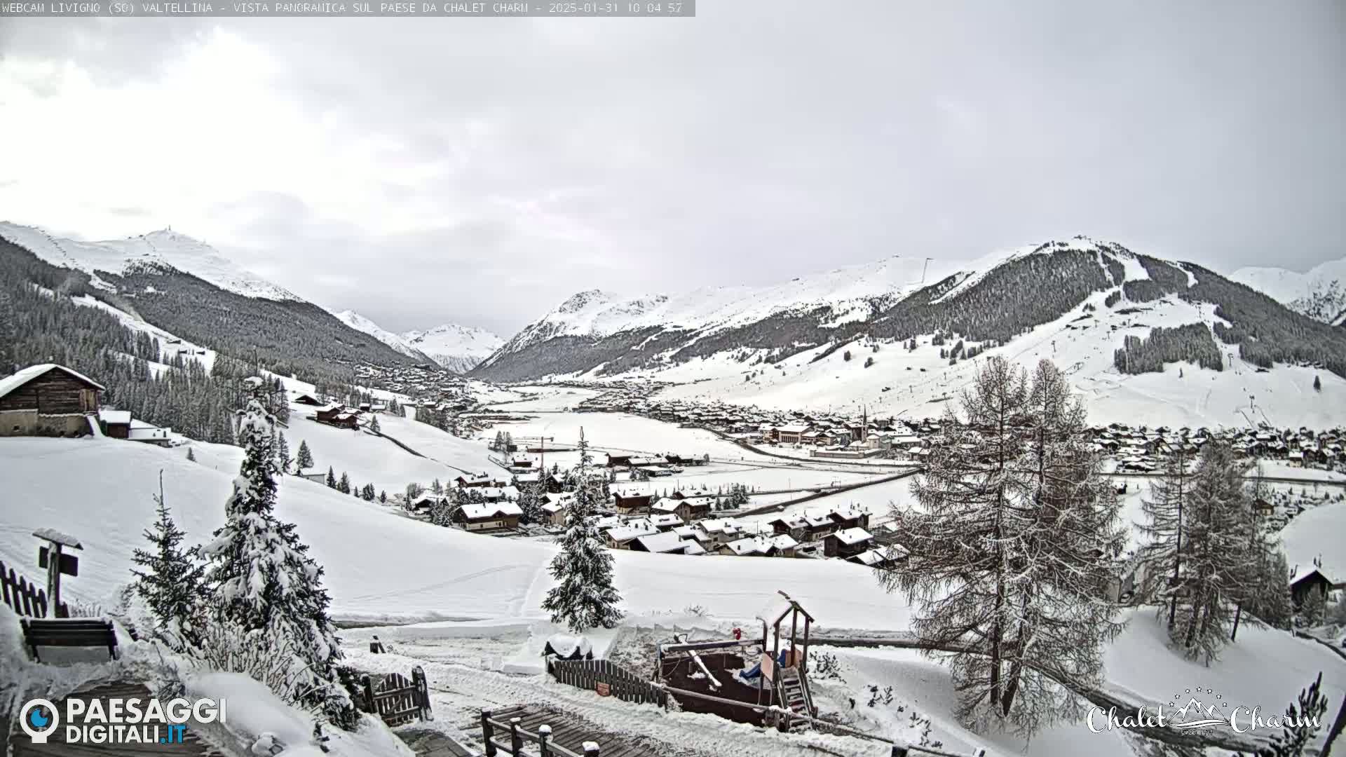A snow-covered village nestled in a valley between snow-capped mountains under an overcast sky.