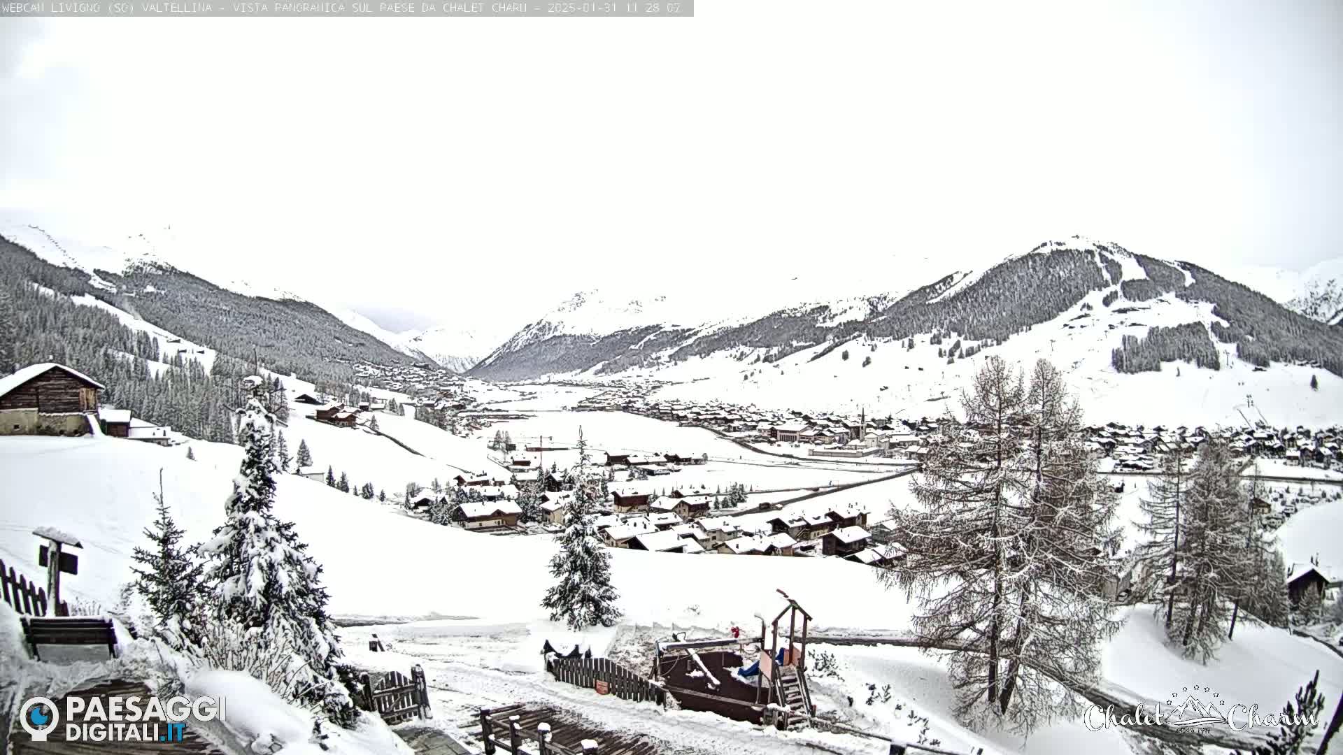 A snow-covered village nestled in a valley between snow-capped mountains under an overcast sky.