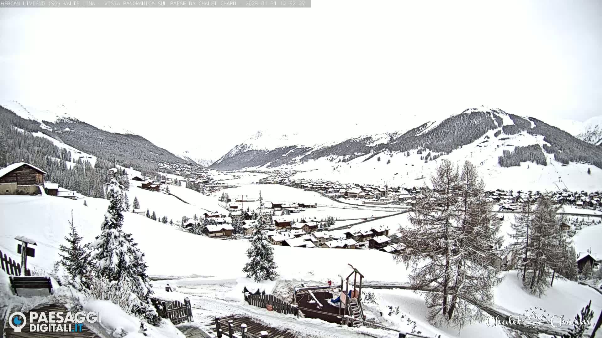A snow-covered village nestled in a valley between snow-capped mountains under an overcast sky.