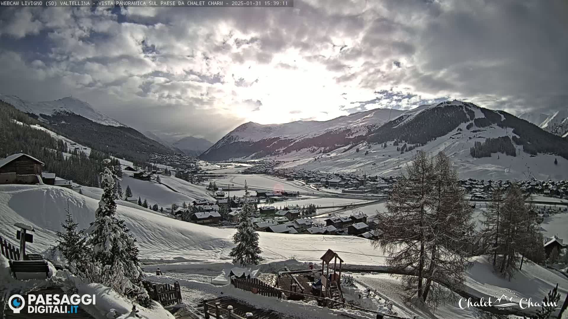 A snow-covered village nestled in a valley between mountains under a partly cloudy sky.