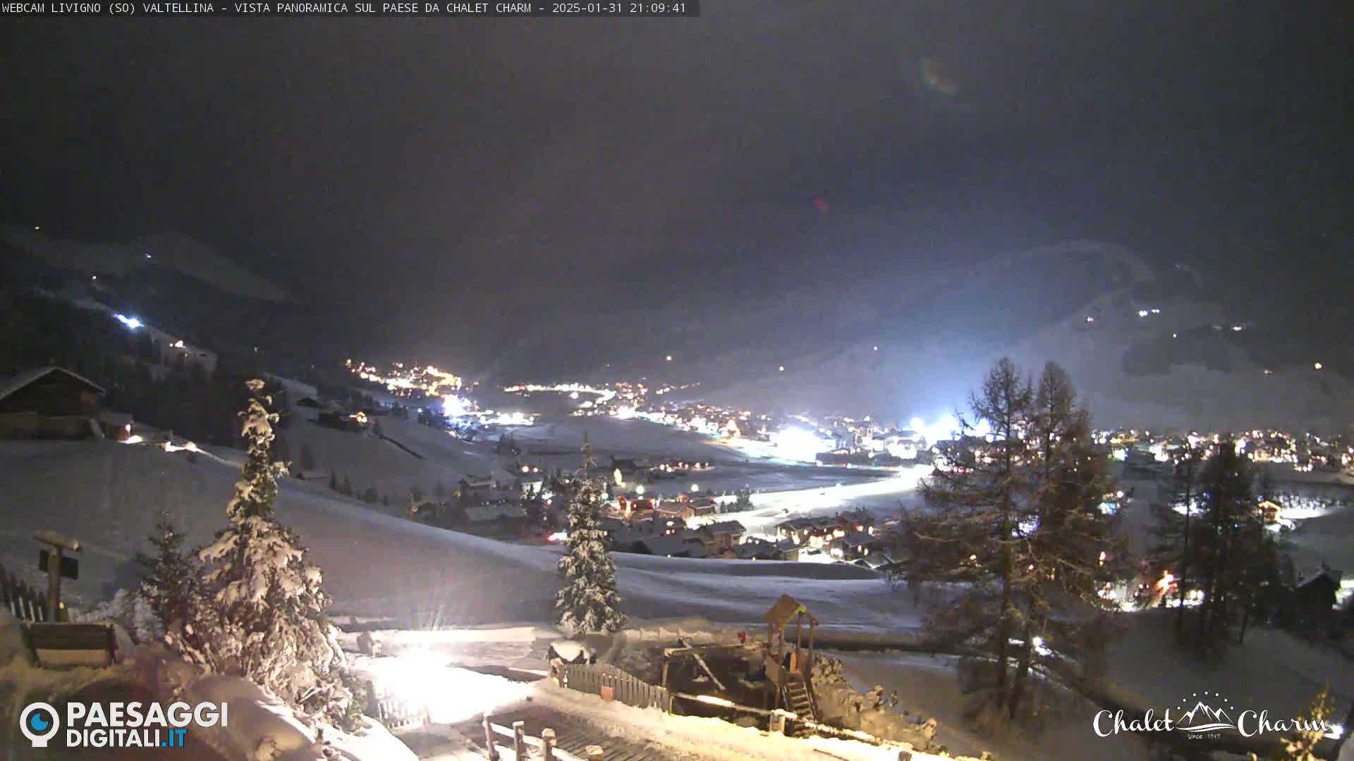 A snow-covered valley town is illuminated at night under a dark sky.