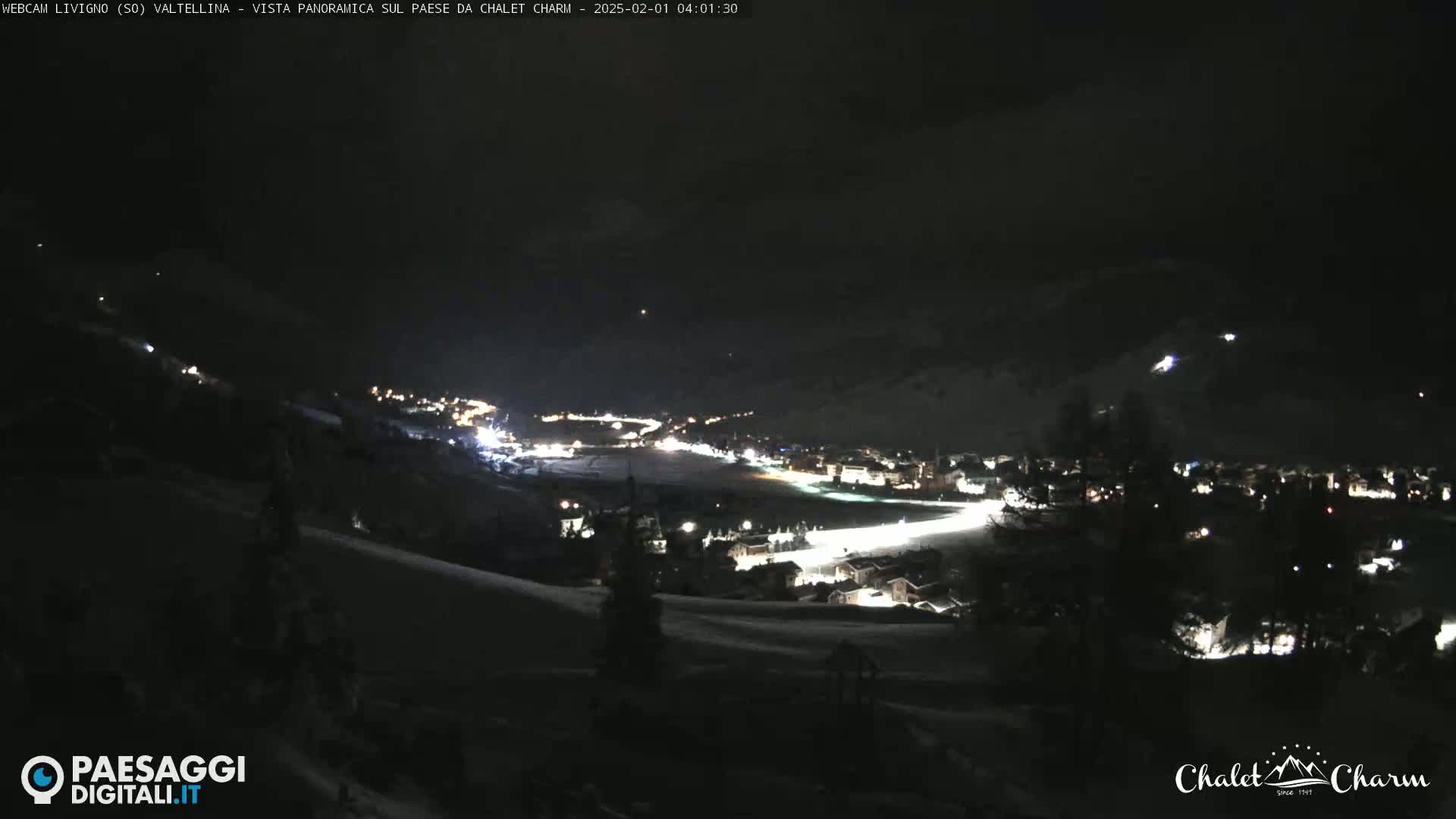 A nighttime, snow-covered landscape reveals a village illuminated with scattered lights below a dark sky.