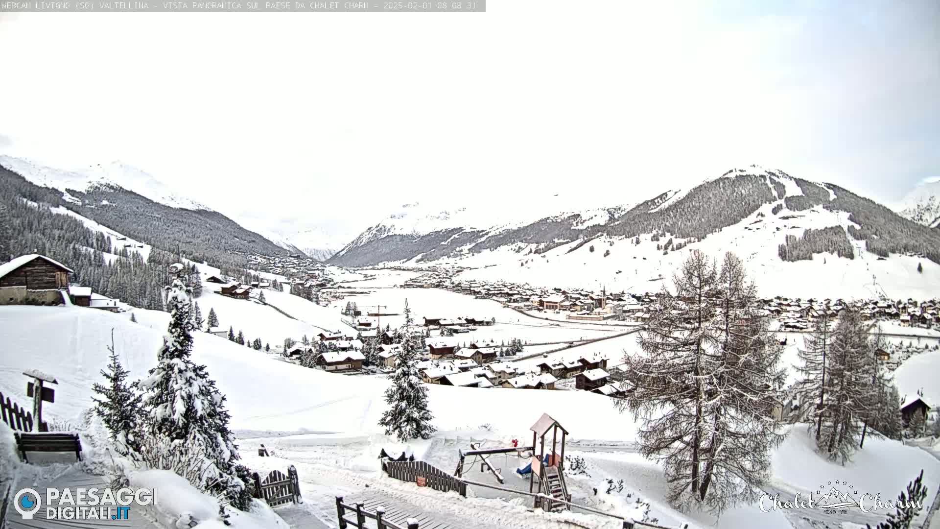 A snow-covered village nestled in a valley between snow-capped mountains under an overcast sky.