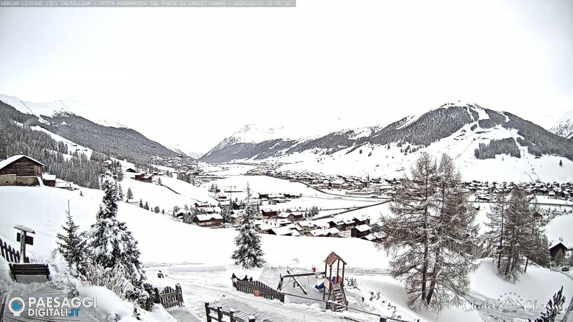A snow-covered village nestled in a valley between snow-capped mountains under an overcast sky.