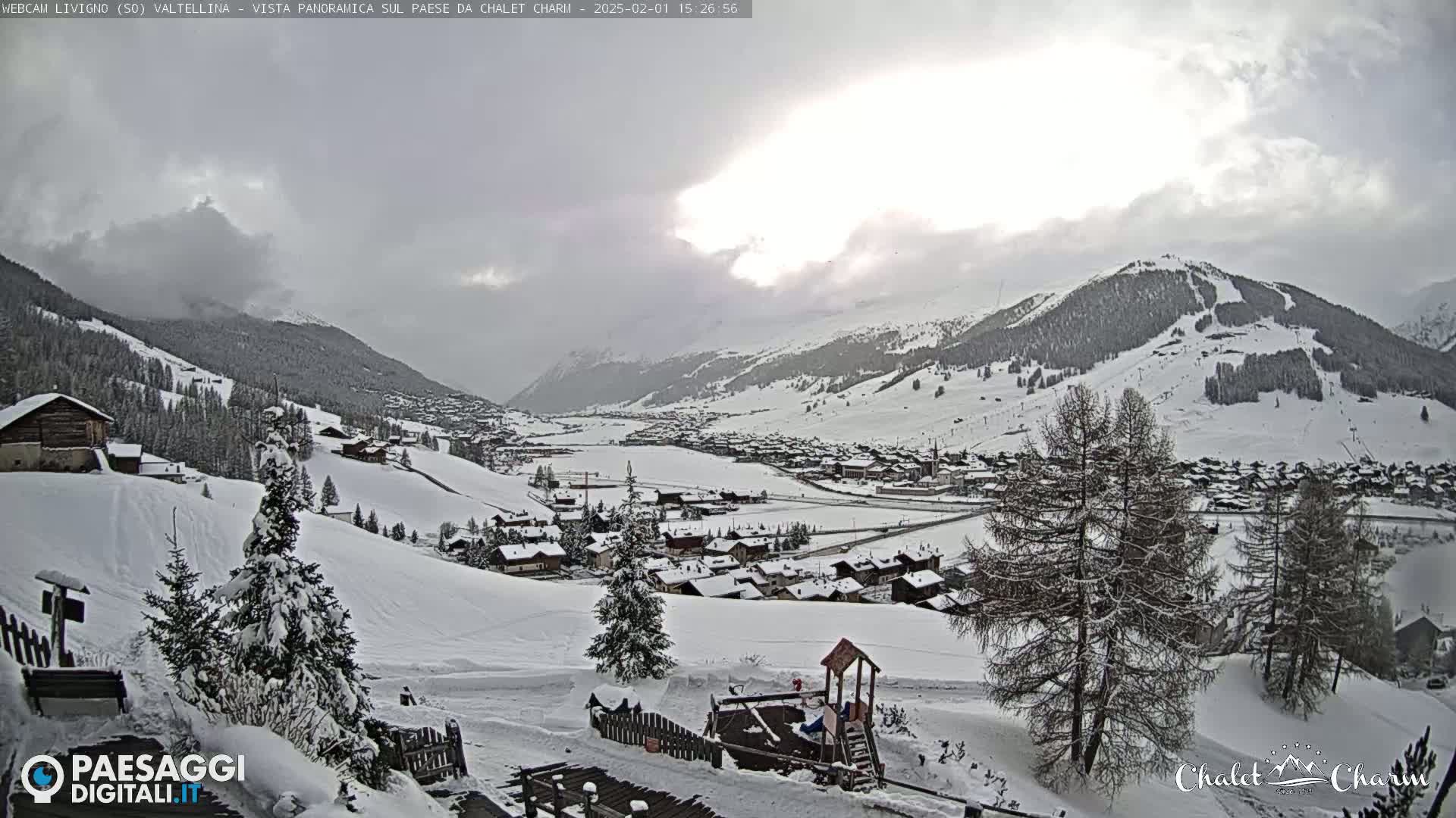 A snow-covered village nestled in a valley between snow-capped mountains under an overcast sky.