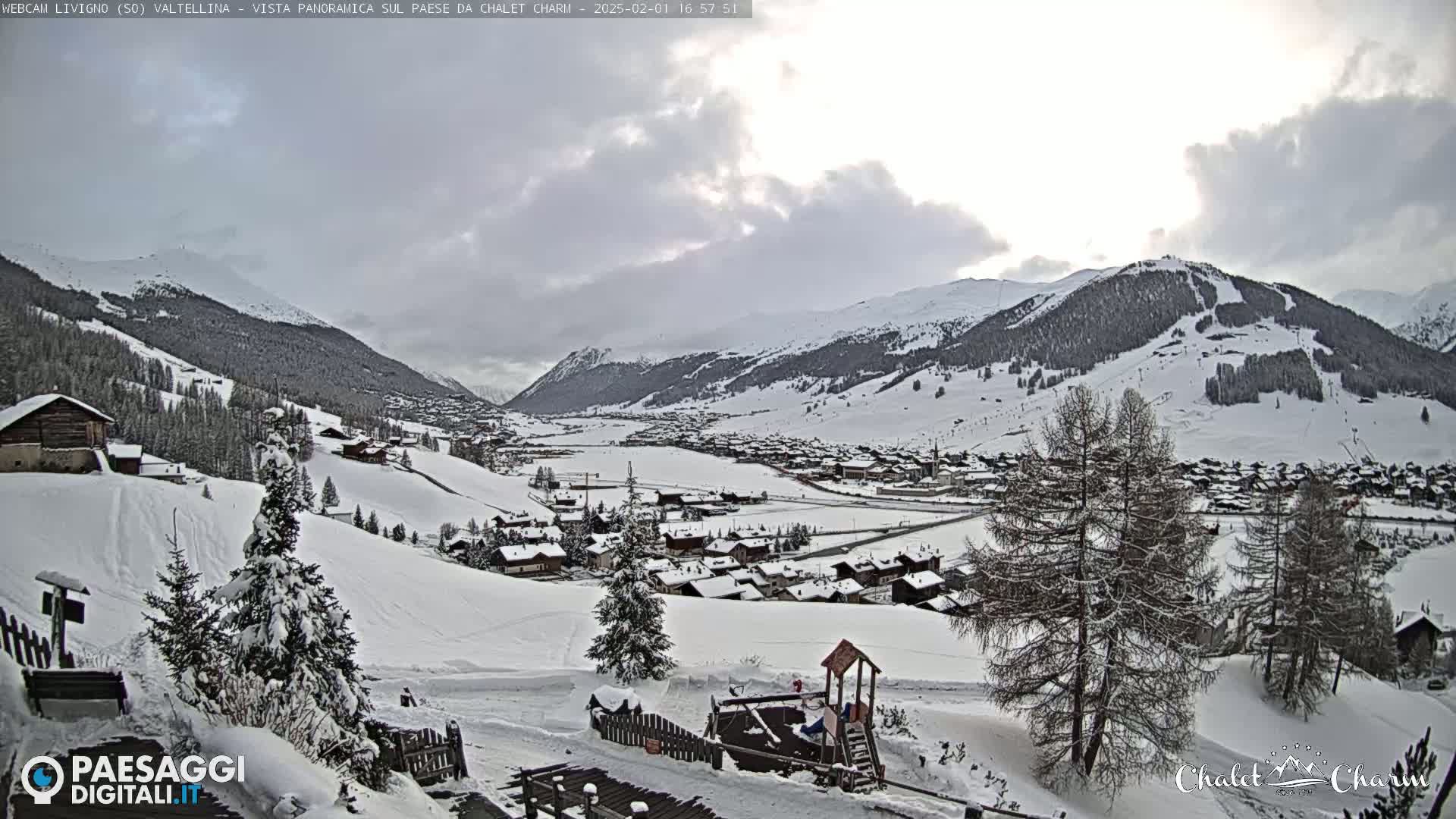 A snow-covered village nestled in a valley between snow-capped mountains under a cloudy sky.