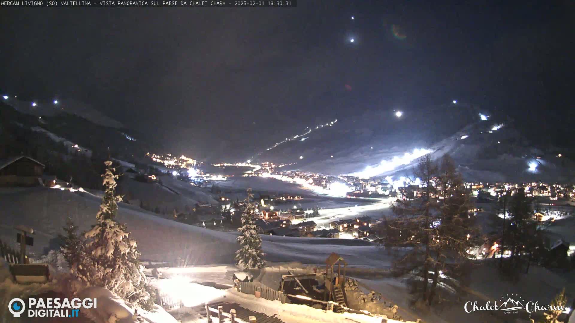 A snow-covered mountain village at night, illuminated by lights, with ski slopes visible on a hillside under a clear, dark sky.