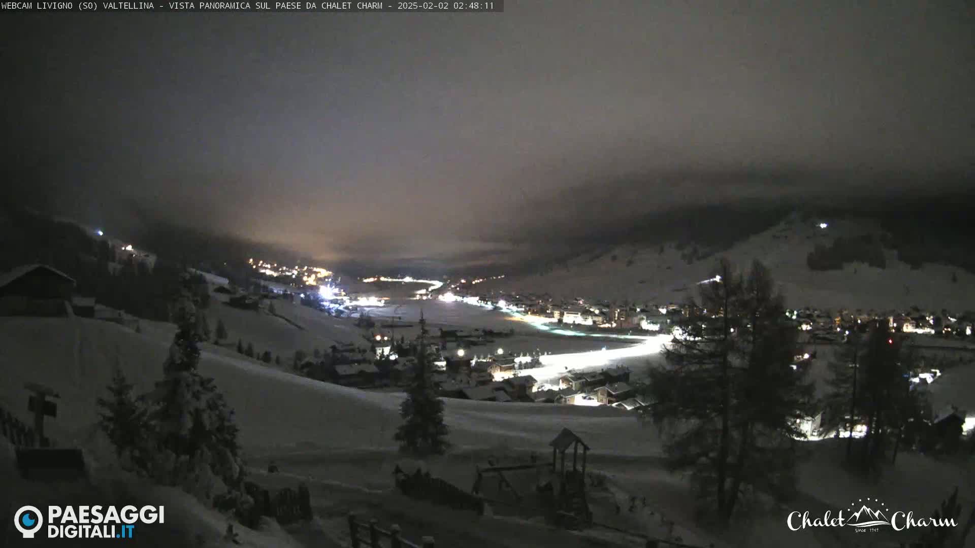 A snow-covered mountain village is illuminated at night under a dark, cloudy sky.
