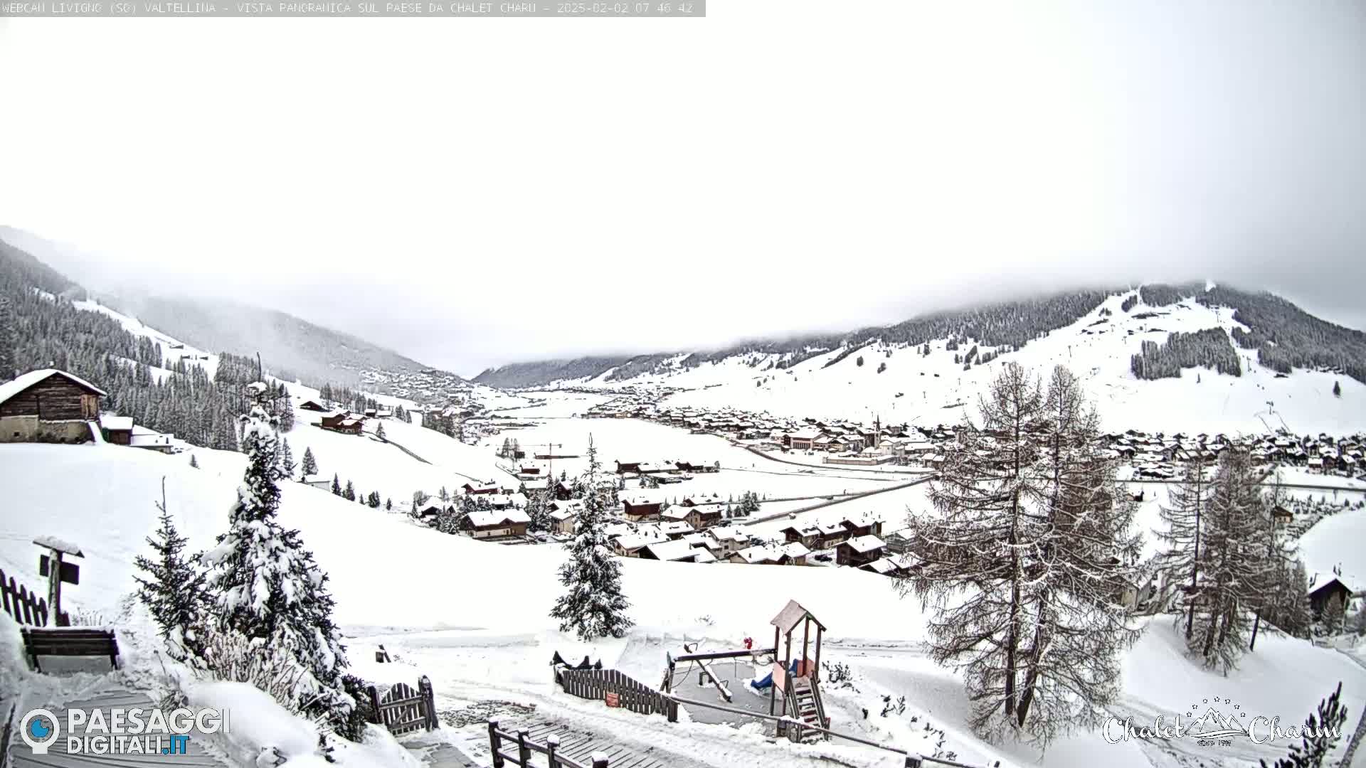 A snow-covered village nestled in a valley, with snow-covered hills and overcast skies in the background.