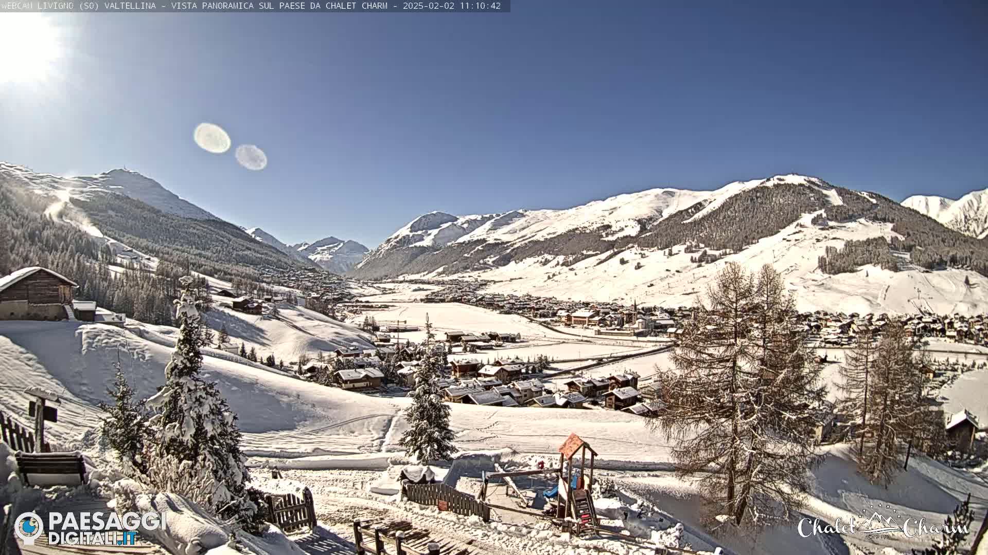A snow-covered village nestled in a valley between snow-capped mountains under a clear, sunny sky.