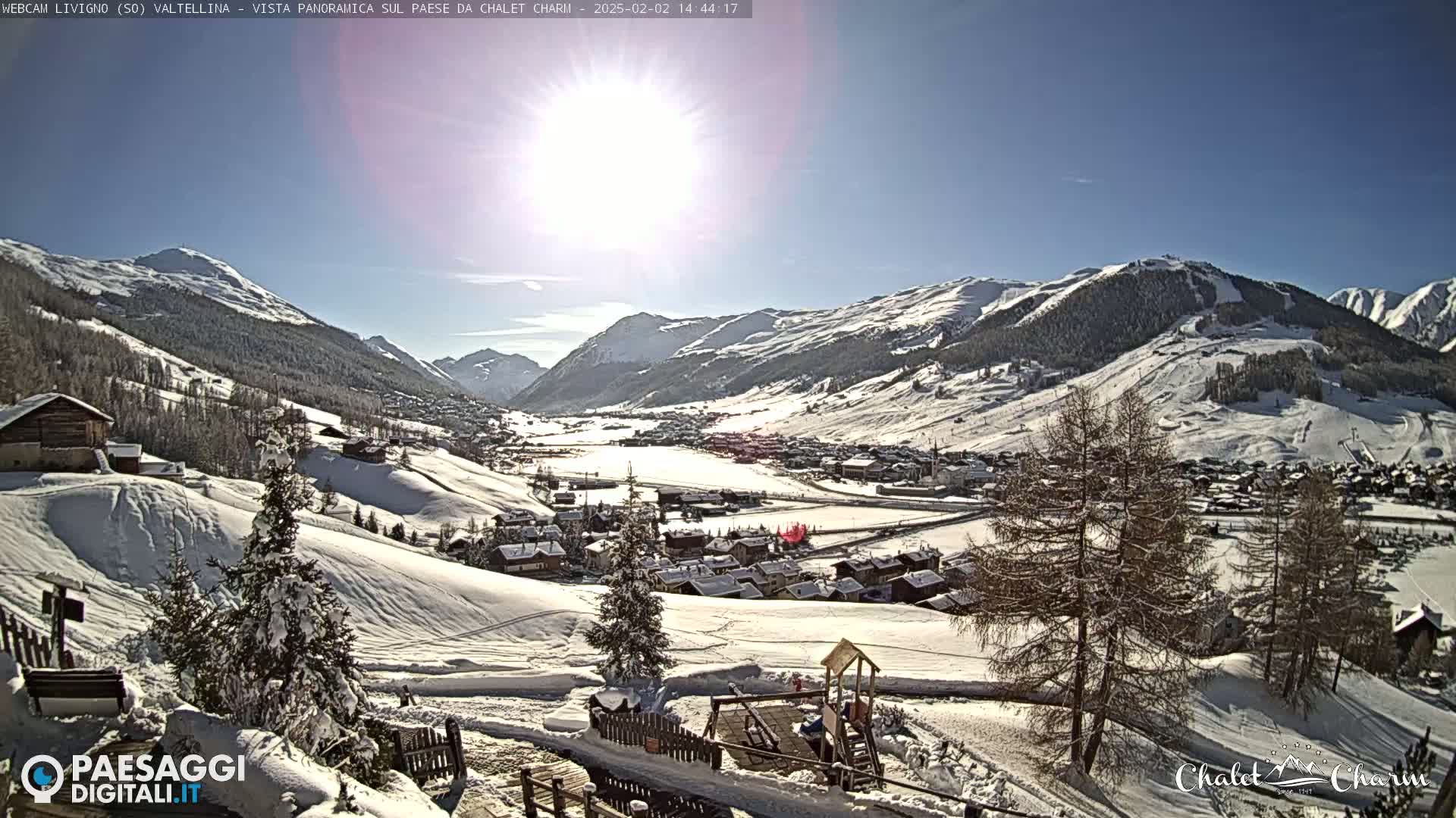 A sunny, snow-covered mountain valley town is viewed from a hillside, with a children's playground visible in the foreground.