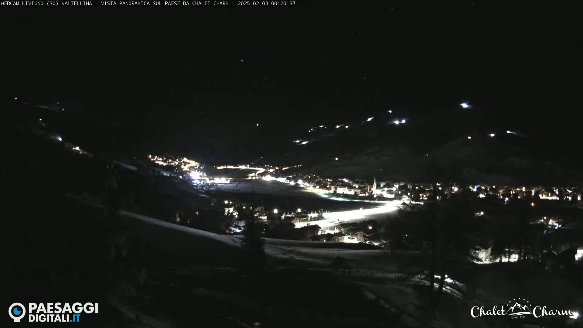 A nighttime, panoramic view of a snow-covered town illuminated by lights, under a clear, starry sky.