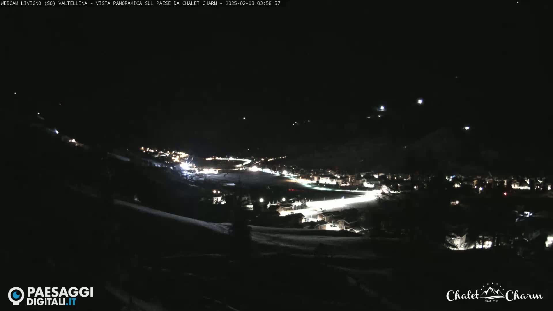 A nighttime, panoramic view of a snow-covered village illuminated by scattered lights under a clear, dark sky.