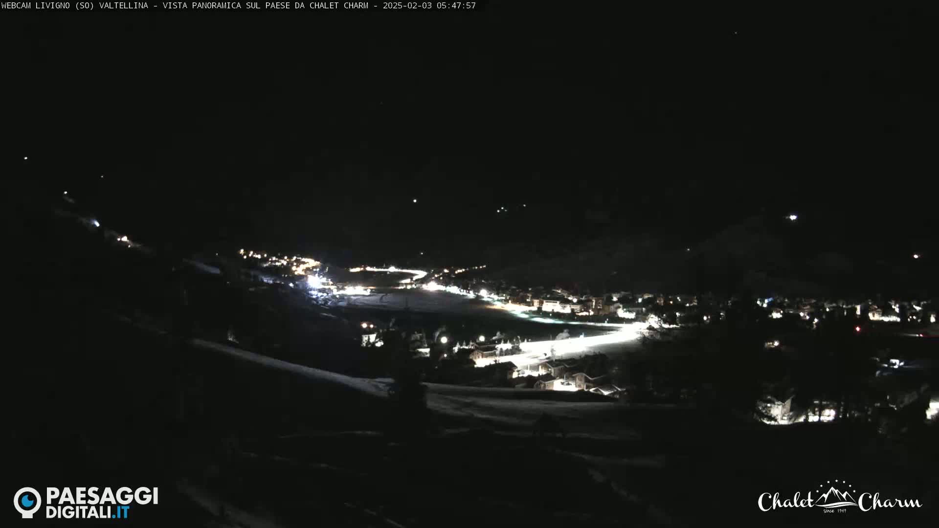 A nighttime, panoramic view of a snow-covered town illuminated by lights, under a clear, dark sky.