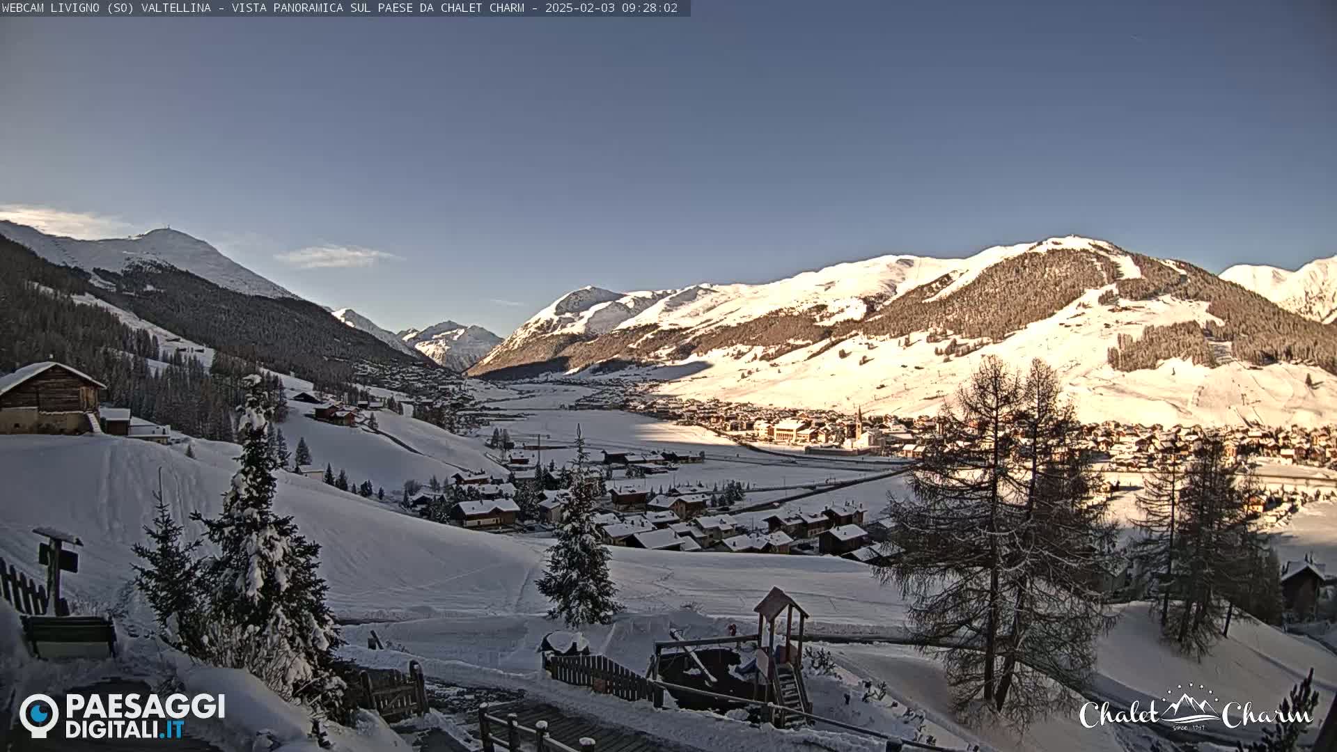 A snow-covered mountain village nestled in a valley between snow-capped mountains under a clear blue sky.