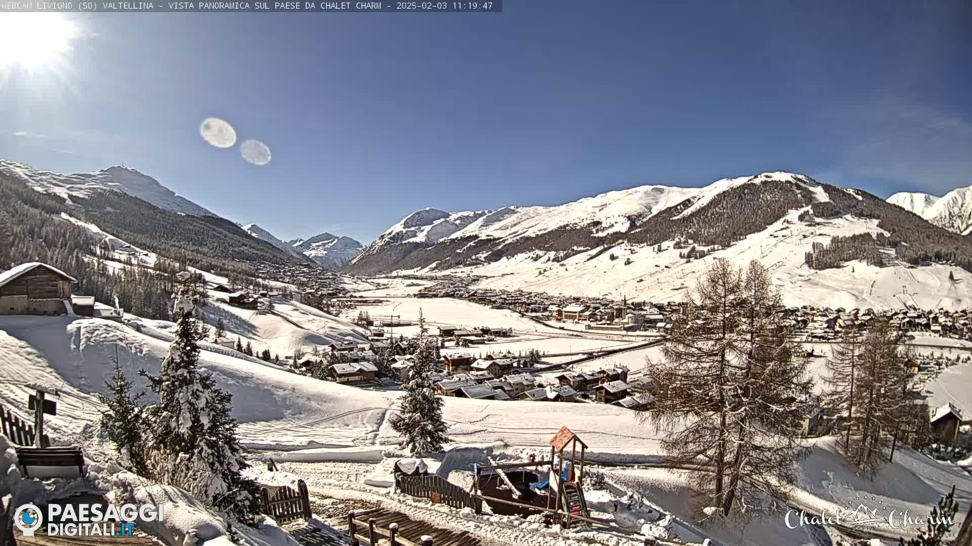 A snow-covered mountain village is nestled in a valley under a clear, sunny sky.