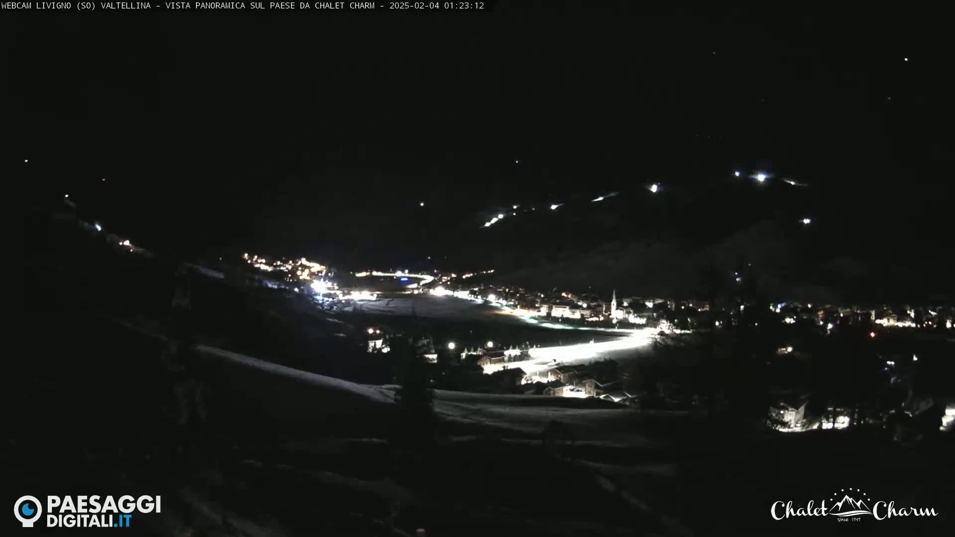 A nighttime, panoramic view of a snow-covered town illuminated by lights, under a dark, clear sky.