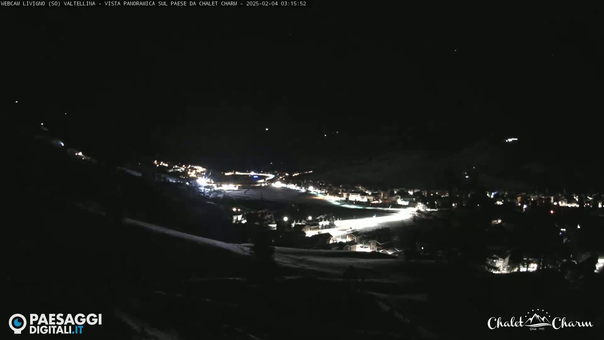 A nighttime, panoramic view of a snow-covered town illuminated by scattered lights under a clear, dark sky.