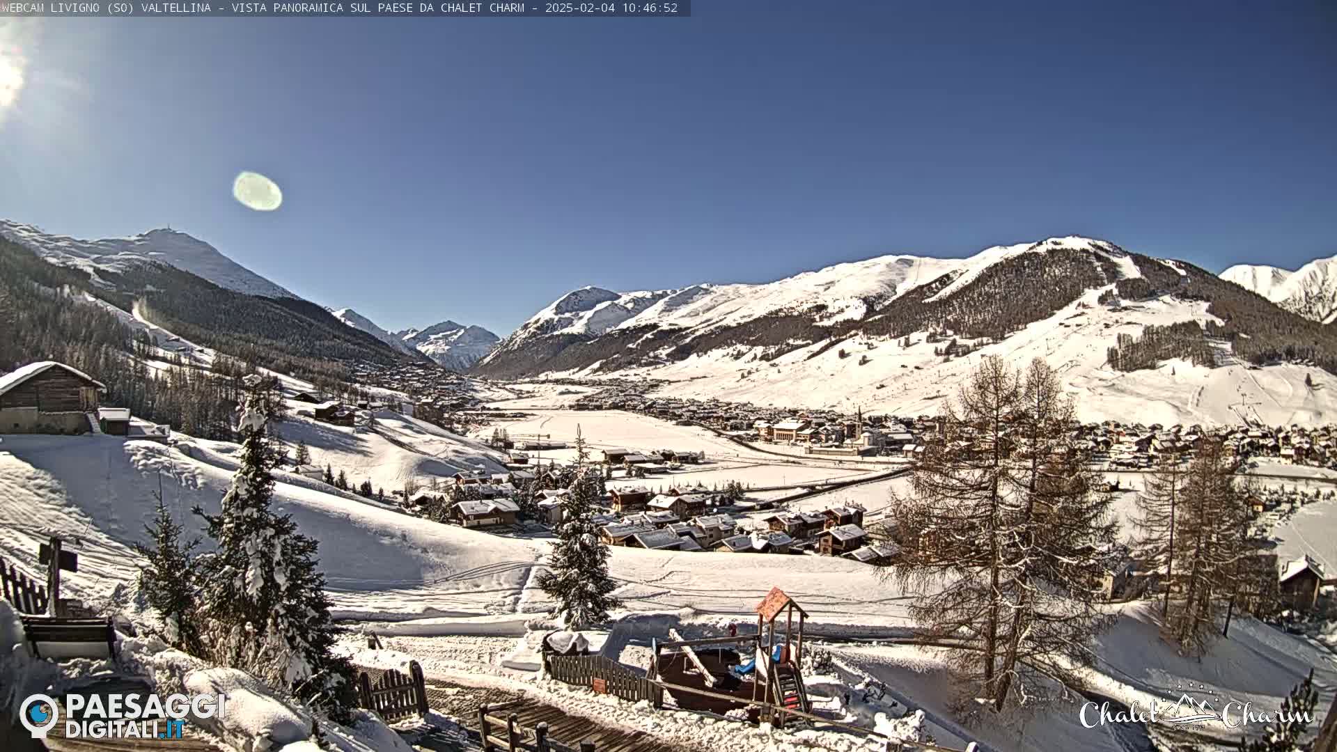 A snow-covered village nestled in a valley between snow-capped mountains under a clear blue sky.