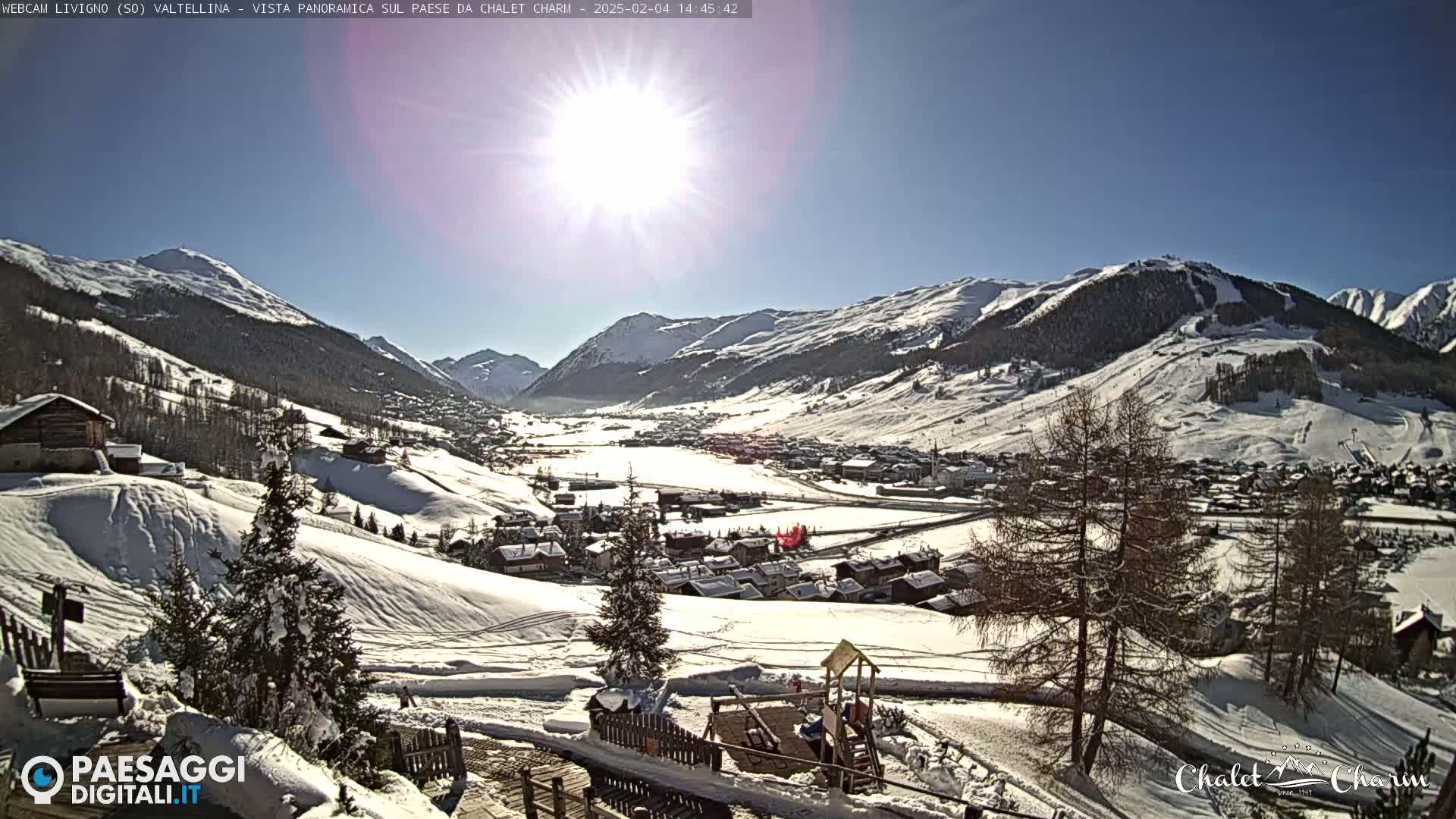 A sunny, snow-covered mountain valley town is viewed from a hillside, with a children's playground in the foreground.